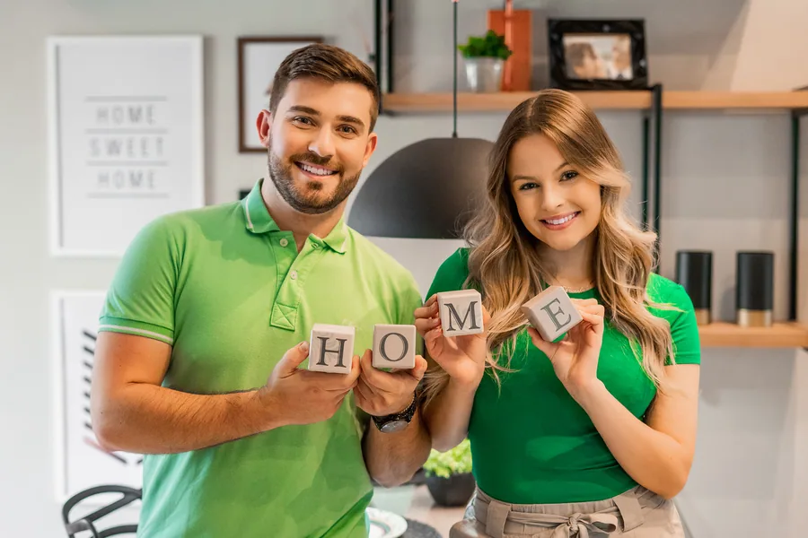 Casal feliz segurando quadrinho escrito HOME ao decorar seu apartamento pequeno